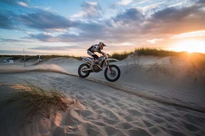 Course de moto spectaculaire sur la plage Moto en plein saut sur une dune de sable au coucher du soleil